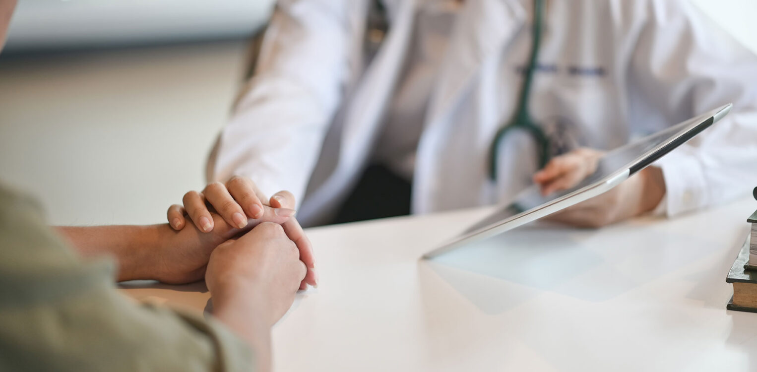 A female doctor holds hands with another woman while holding a tablet