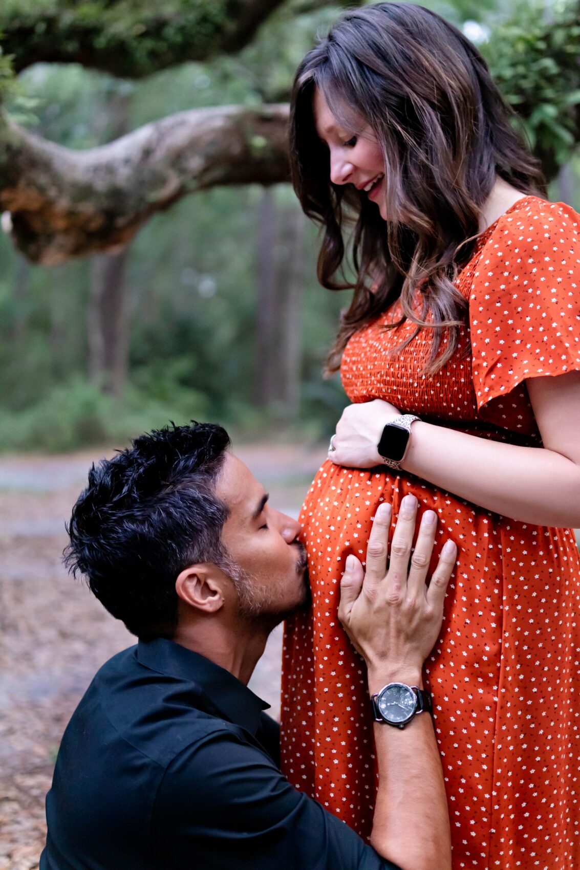 A man kneels down and kisses a pregnant woman's belly