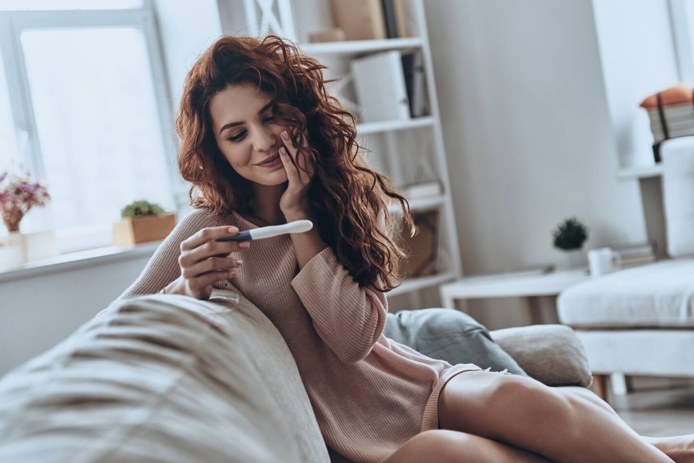 A young woman smiles as she looks at a pregnancy test she is holding up